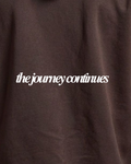 Close-up of a dark brown textured fabric with the phrase 'the journey continues' printed in white script across the center.