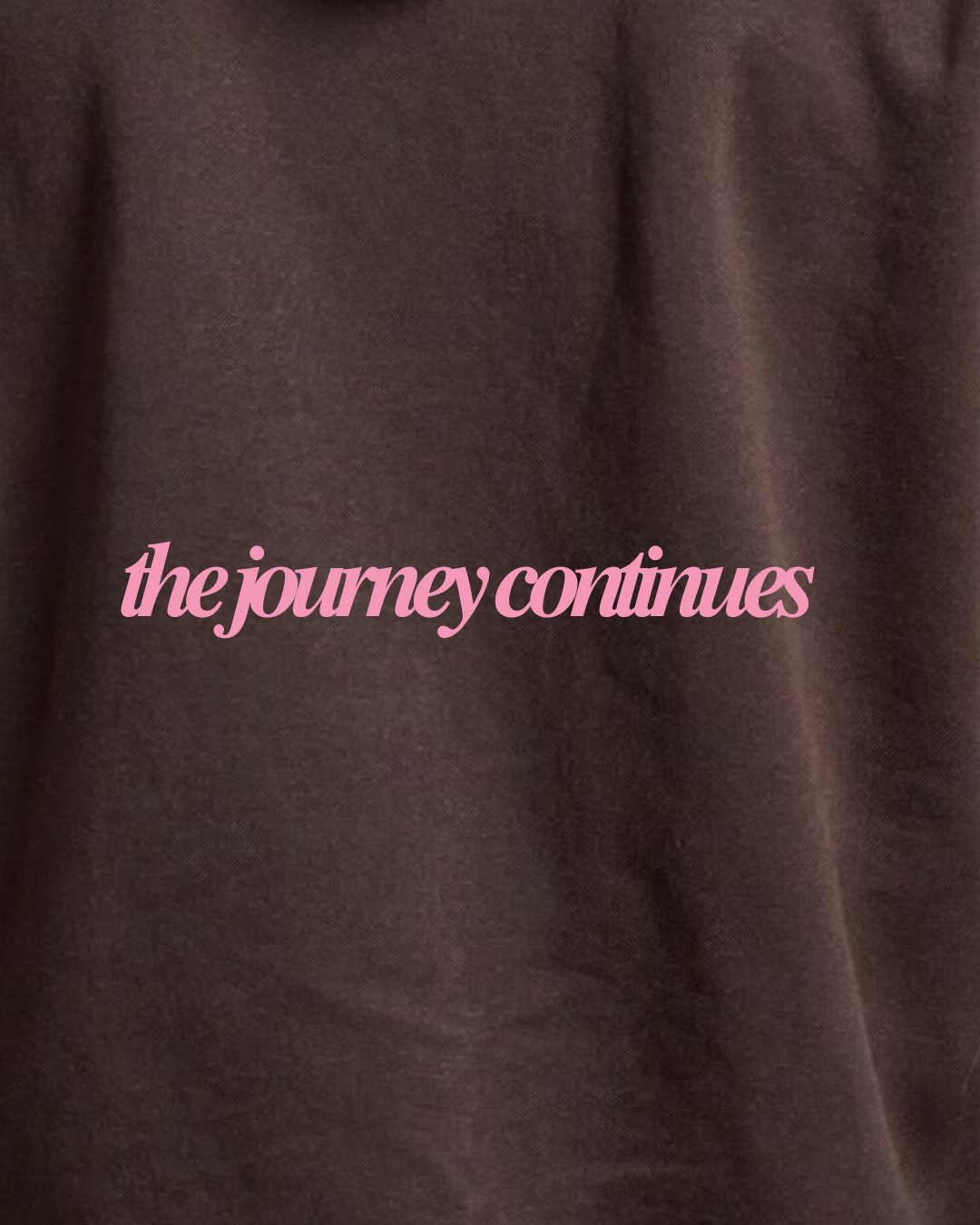 Close-up of a dark brown fabric surface with pink script text reading 'the journey continues' across the center.