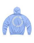 A light blue hoodie shown from the back, featuring a large white circular text graphic that reads 'the journey continues ' across the back.